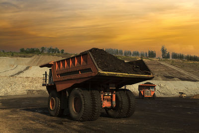 Vehicle on dirt road against sky during sunset