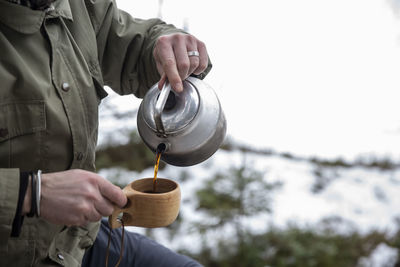 Midsection of mature man pouring tea in wooden cup from kettle