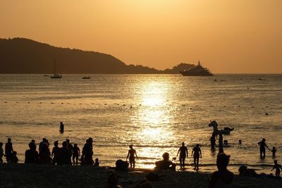 Silhouette people on beach against sky during sunset