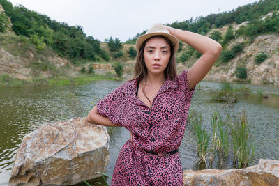 Portrait of beautiful young woman standing on rock by the lake 
