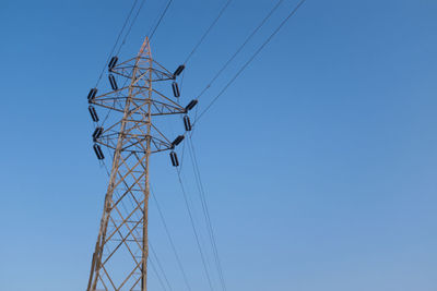 Low angle view of electricity pylon against clear blue sky