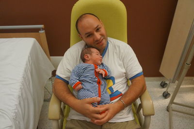 High angle portrait of father with newborn baby on chair at hospital