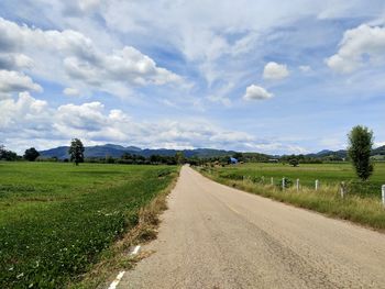 Dirt road amidst field against sky