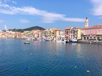 Sailboats in sea by town against sky