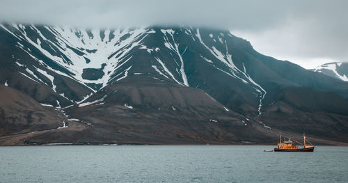 Scenic view of sea by snowcapped mountains against sky