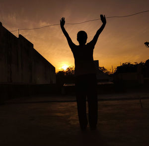 Silhouette man standing by building against sky during sunset