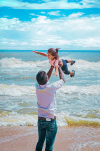 Father playing with daughter at beach against sea and sky