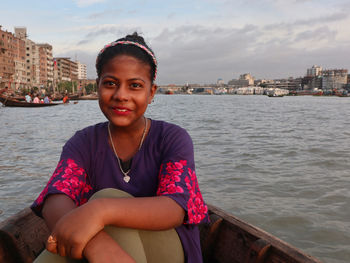 Portrait of smiling woman sitting on sea against cityscape