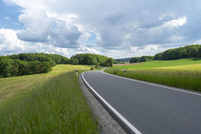 Empty road amidst field against sky