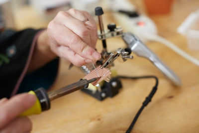 Cropped hands of female technician soldering metal on equipment at workshop