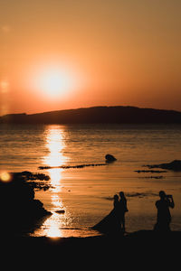 Silhouette people on beach against sky during sunset