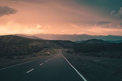 Road leading towards mountains against sky at sunset