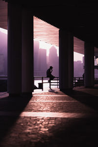 Silhouette man sitting on railing in corridor of building