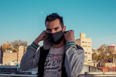 Portrait of young man with face mask in city against clear sky