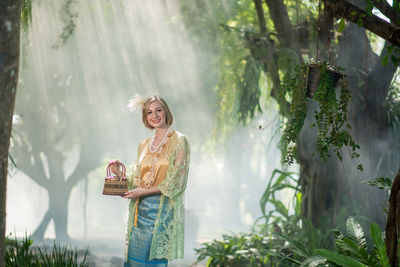 Woman standing by plants against trees