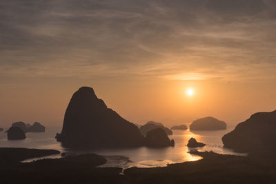 Rocks in sea against sky during sunset