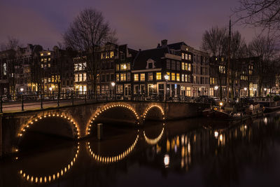 Arch bridge over river by buildings at night