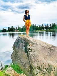 Man standing on rock by lake against sky