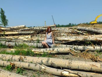 Portrait of woman sitting on logs against clear sky