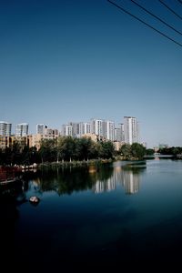 Buildings by lake against clear blue sky