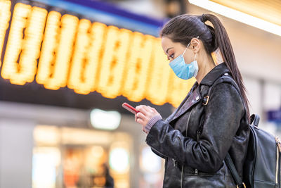 Woman holding mobile phone looking away while standing on street