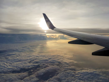 Picture of wing of airplane flying above the clouds with sun from window in the morning