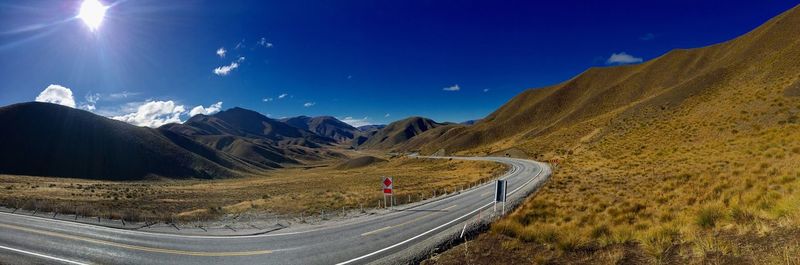 Road leading towards mountains against blue sky during sunny day