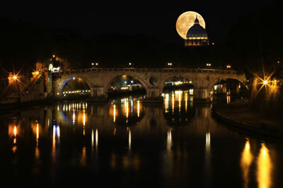 Illuminated bridge over tevere river with full moon behind st. peter's at night