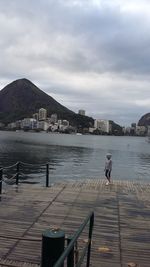 Person on pier by sea against sky in city