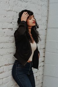 Young woman looking down while standing against wall