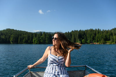 Smiling woman sitting in boat at lake against sky