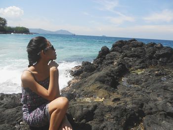 Girl sitting on rock at beach against sky