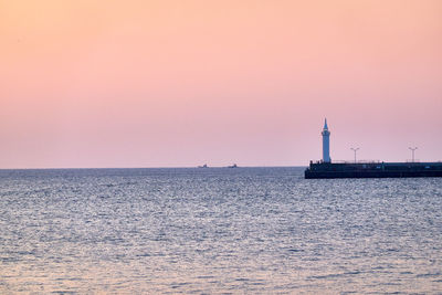 Lighthouse by sea against sky during sunset