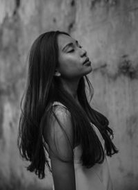 Mid adult woman with eyes closed standing against wall outdoors