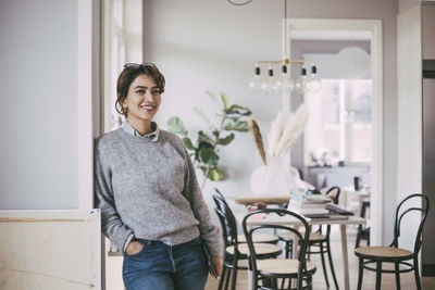 Portrait of smiling young woman standing against wall