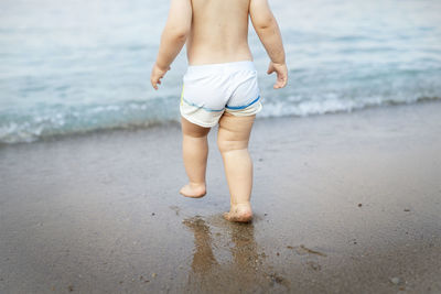 Low section of shirtless boy walking on shore at beach