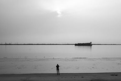 Rear view of man standing at beach against clear sky