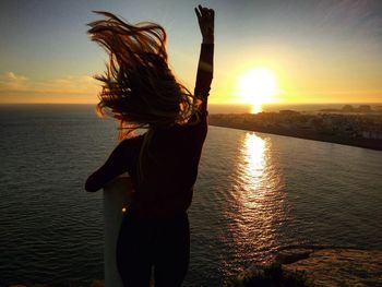 Woman standing in sea against sky during sunset