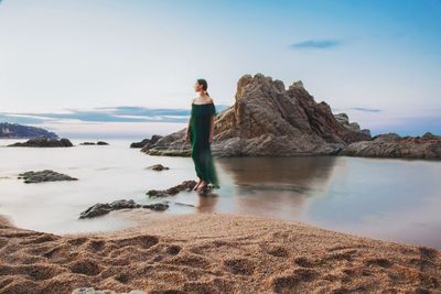 Young woman standing on rock at sea shore against sky