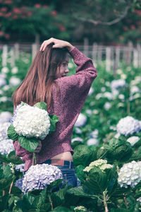 Rear view of woman holding flowers while standing by plants