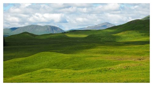 Scenic view of green landscape and mountains against sky