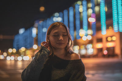 Portrait of young woman looking at illuminated city at night