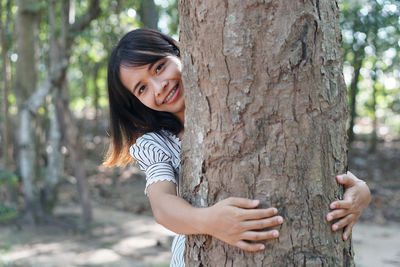 Portrait of a smiling young woman against tree trunk