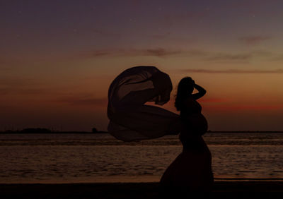 Silhouette man standing at beach against sky during sunset