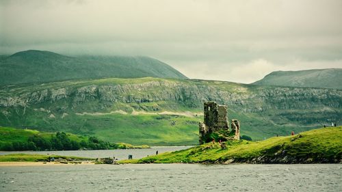 Ardvreck castle by lake against cloudy sky