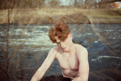 Portrait of shirtless man against river