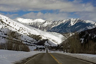 Road leading towards snowcapped mountains against sky