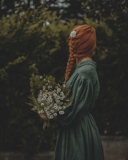 Rear view of woman standing by flowering plant