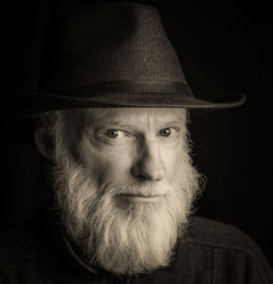 Close-up portrait of man wearing hat against black background