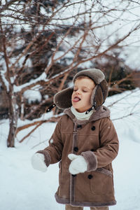 A boy in a winter hat and coat rejoices in the snow. the child catches snowflakes with his tongue. 